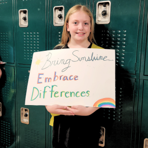 student standing in front of lockers holding a poster