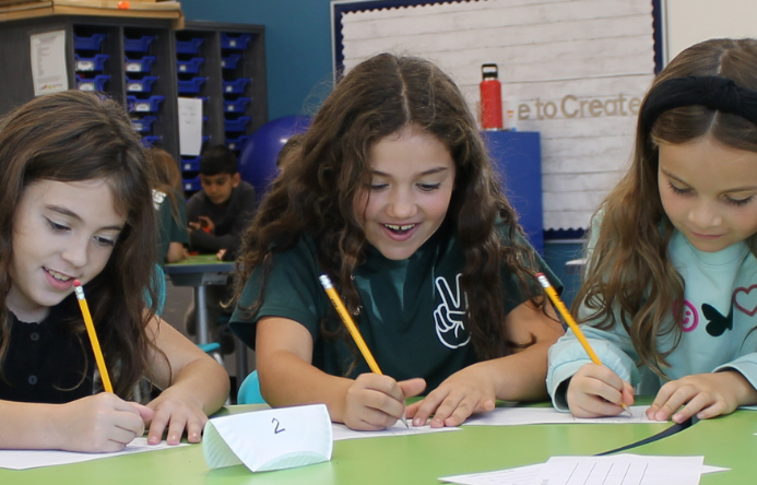 three students sitting at a table writing