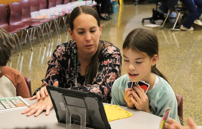 a student and teacher sitting at a table with a tablet in front of them