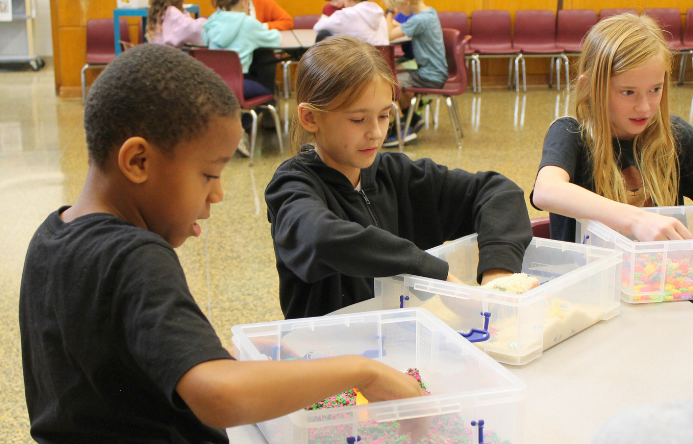 three students putting their hands into sensory bins