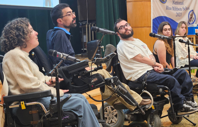 a group of panelists, some in wheelchairs, speaking into microphones