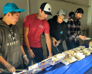 Four members of Patriot Club standing behind a table lined with donuts, ready to serve veterans