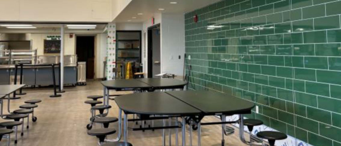 square tables next to a newly green-tiled wall in the high school cafeteria