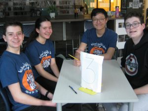 four students sitting at a table in the library and smiling for a picture