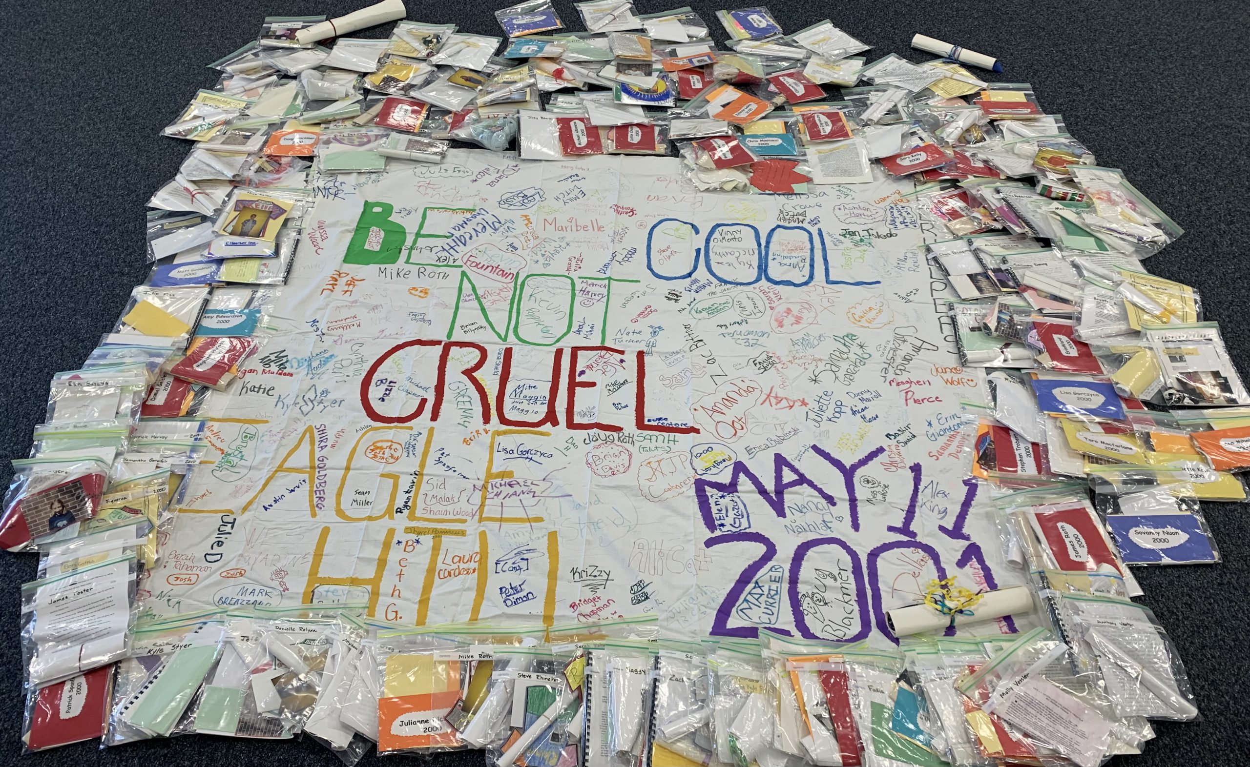 A sheet with writing on it that says "Be Cool Not Cruel, Eagle Hill, May 11, 2001." Surrounding the sheet are dozens of Ziploc bags filled with items